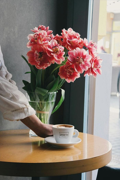 Caféägare ställer fram en kaffe på ett bord med tulpaner.